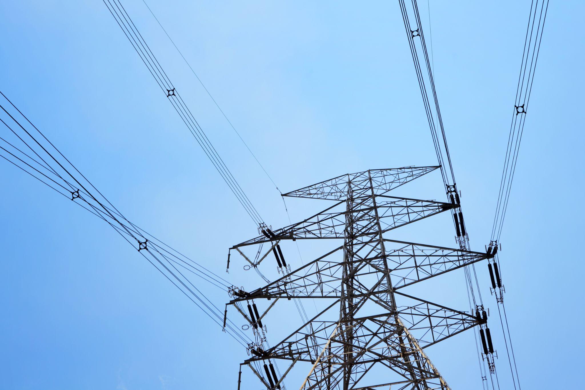 High-voltage power lines and a utility tower against a blue sky, representing external sources of power surges in the Lower Mainland.