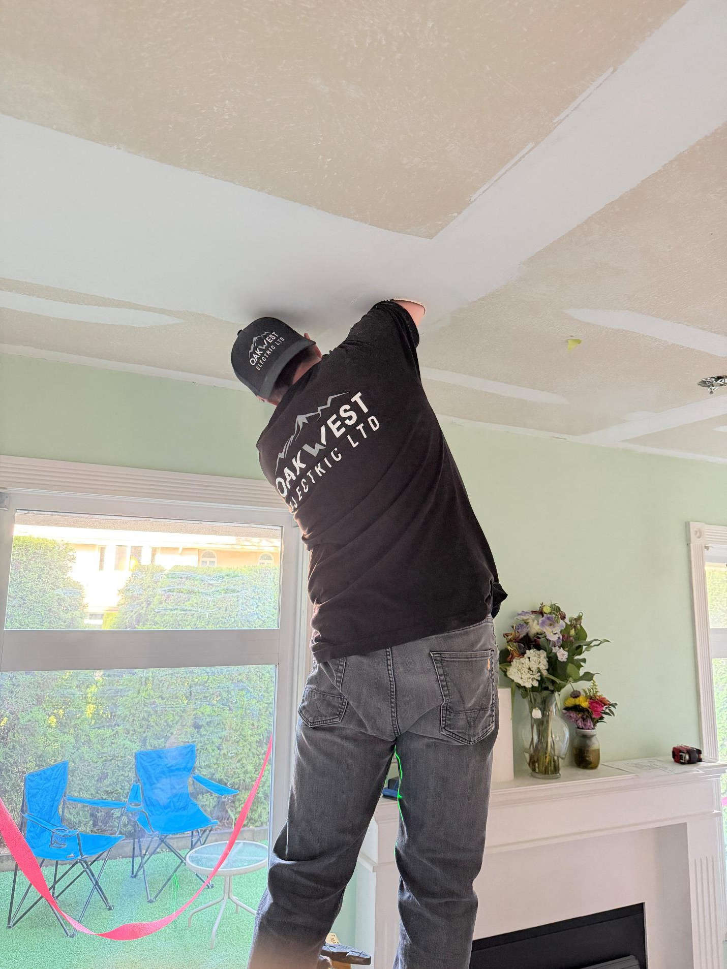 An Oakwest Electrician performing a lighting upgrade by installing wiring through a clean ceiling cut to show how do lighting upgrades actually make a difference with minimal disruption.