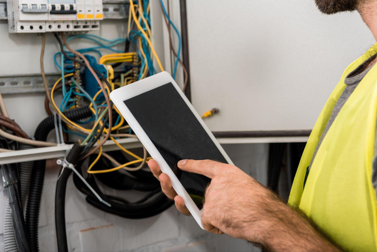 An electrician using a digital tablet to inspect a modern electrical panel while performing a heritage home rewiring project.