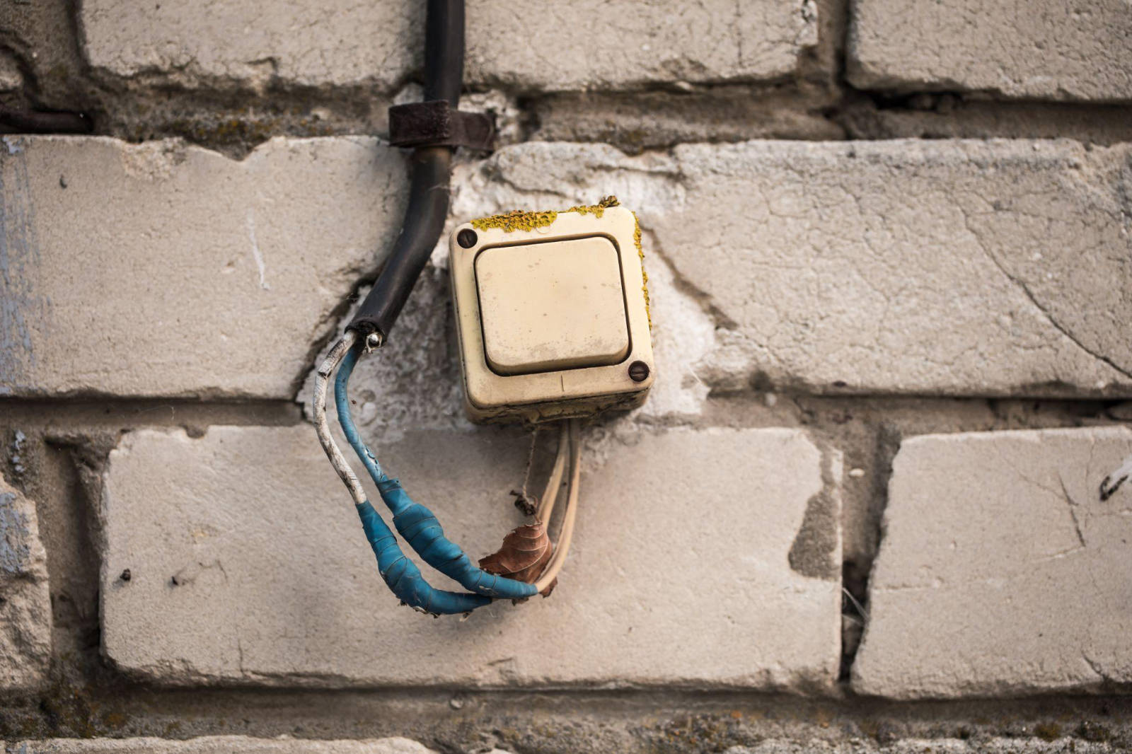 A close-up of an old, yellowed light switch mounted on a brick wall with exposed wiring, representative of outdated electrical systems in heritage homes.