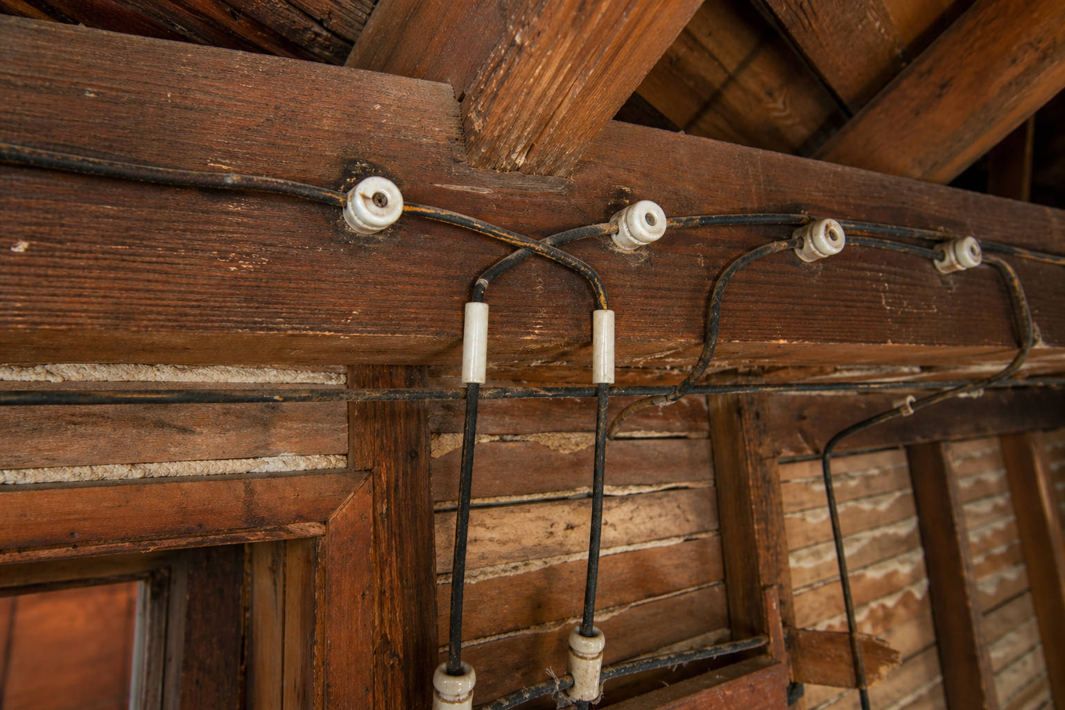 Vintage knob-and-tube electrical wiring attached to a wooden beam in a heritage home, highlighting historical electrical infrastructure.