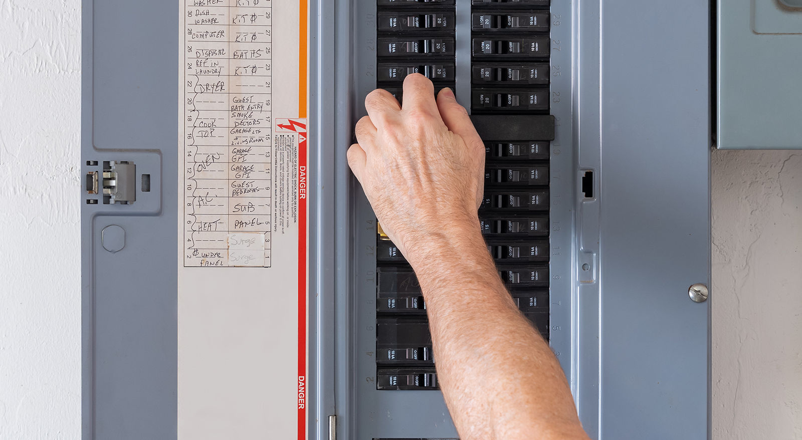 Hand flipping a switch inside a home electrical breaker panel to demonstrate troubleshooting tripped circuits.